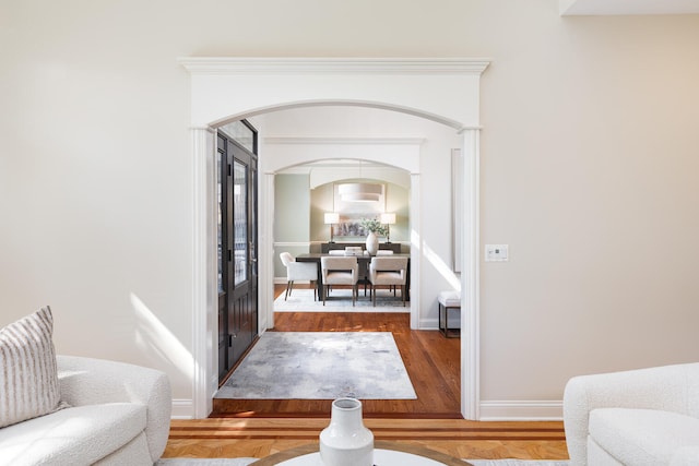 sitting room with arched walkways, wood finished floors, and baseboards