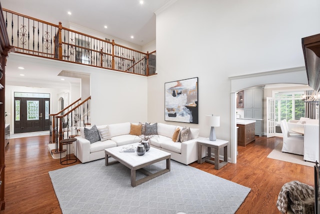 living area with arched walkways, stairway, crown molding, plenty of natural light, and a towering ceiling