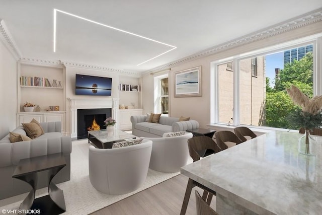 living room featuring wood finished floors, a warm lit fireplace, and built in features