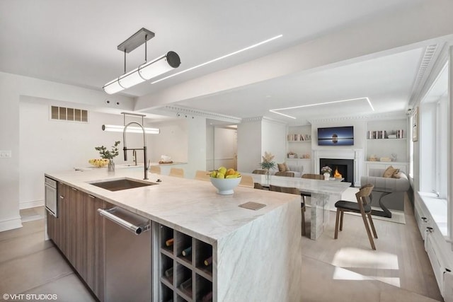 kitchen featuring a sink, dishwasher, modern cabinets, a kitchen island with sink, and light stone counters