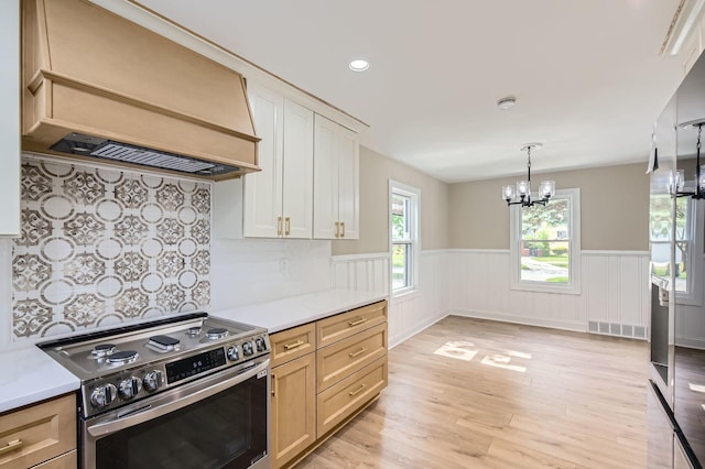 kitchen with stainless steel range with electric stovetop, premium range hood, a chandelier, a wainscoted wall, and light countertops
