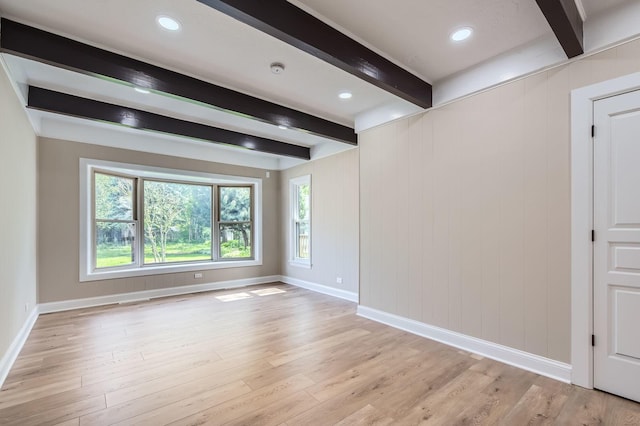 empty room featuring beam ceiling, baseboards, and light wood-style floors