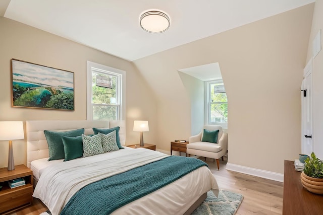 bedroom with multiple windows, light wood-type flooring, baseboards, and lofted ceiling