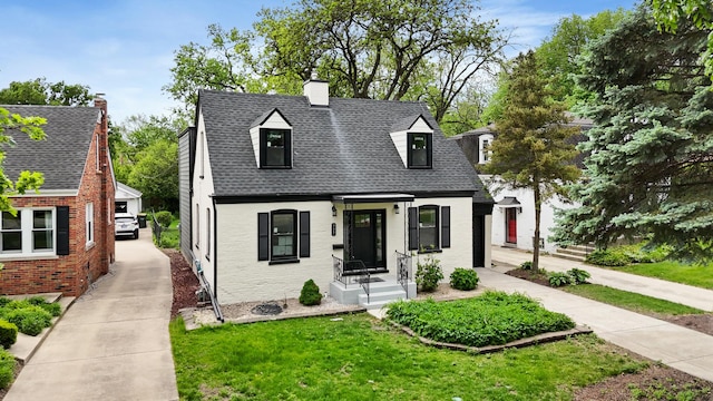 view of front of property featuring brick siding, a front yard, a shingled roof, and a chimney