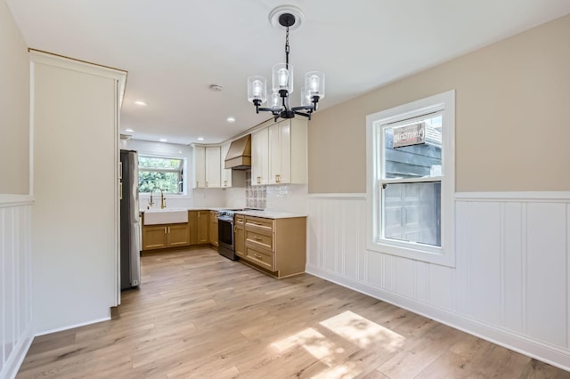 kitchen featuring appliances with stainless steel finishes, custom range hood, a chandelier, a sink, and wainscoting
