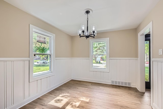 empty room with a wainscoted wall, a chandelier, wood finished floors, and a decorative wall