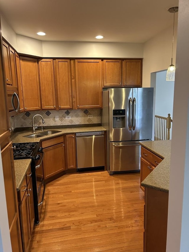 kitchen featuring appliances with stainless steel finishes, a sink, light wood-type flooring, brown cabinets, and recessed lighting