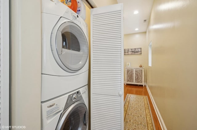 clothes washing area with stacked washing machine and dryer, baseboards, wood finished floors, and recessed lighting