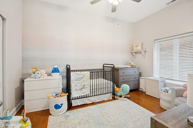 bedroom with a nursery area, wood finished floors, and ceiling fan