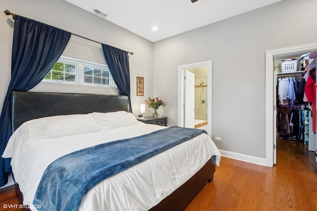 bedroom with wood finished floors, a walk in closet, baseboards, a closet, and connected bathroom