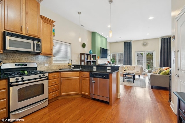 kitchen featuring stainless steel appliances, a peninsula, a sink, light wood-style floors, and open floor plan