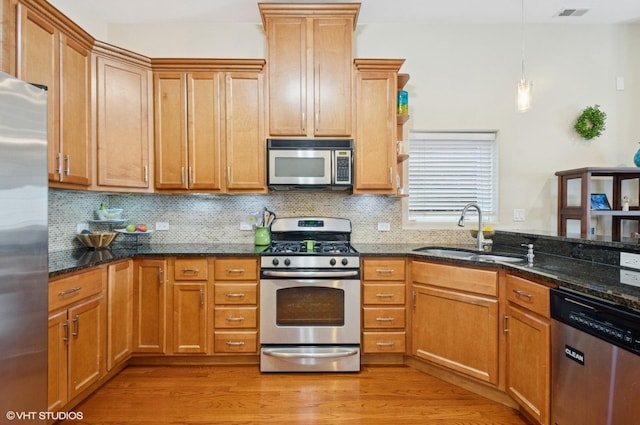 kitchen featuring stainless steel appliances, a sink, light wood-style floors, backsplash, and dark stone counters