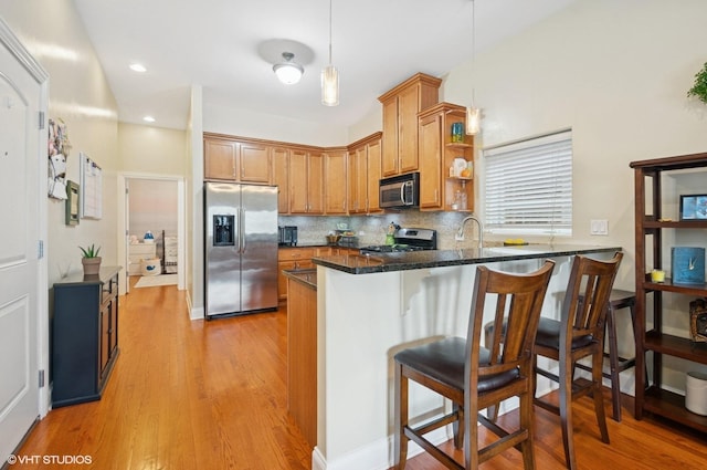 kitchen with appliances with stainless steel finishes, brown cabinets, light wood-type flooring, a peninsula, and a kitchen bar