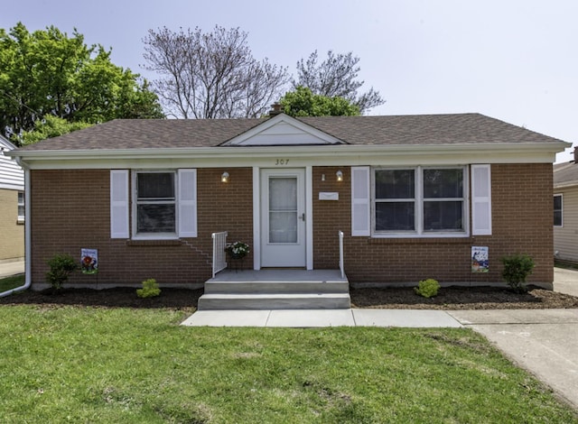 view of front of property with a front yard, brick siding, and roof with shingles