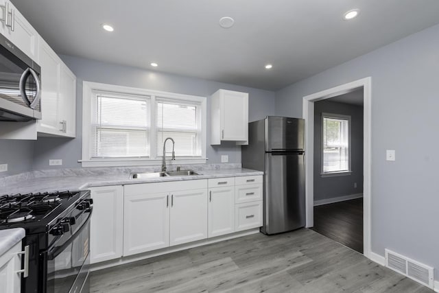 kitchen with a sink, appliances with stainless steel finishes, light countertops, white cabinetry, and recessed lighting