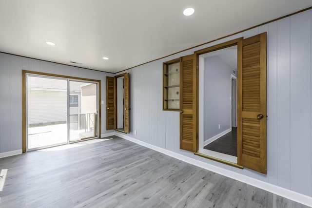 spare room featuring a decorative wall, wood finished floors, baseboards, and recessed lighting