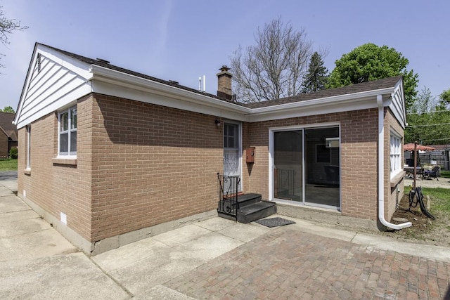 back of house featuring brick siding, a chimney, and a patio