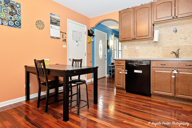 kitchen featuring dishwasher, dark wood-style flooring, decorative backsplash, arched walkways, and light countertops