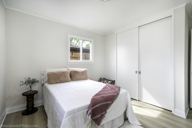 bedroom with light wood-style flooring, a closet, ornamental molding, and baseboards