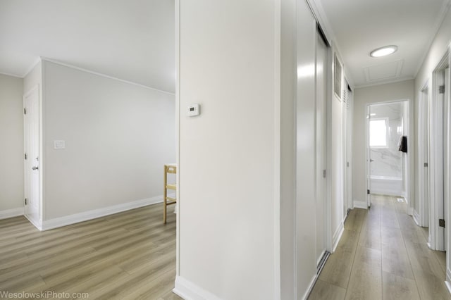hall with light wood-type flooring, crown molding, and baseboards