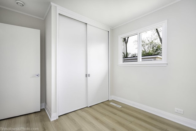 unfurnished bedroom with crown molding, a closet, light wood-type flooring, and baseboards