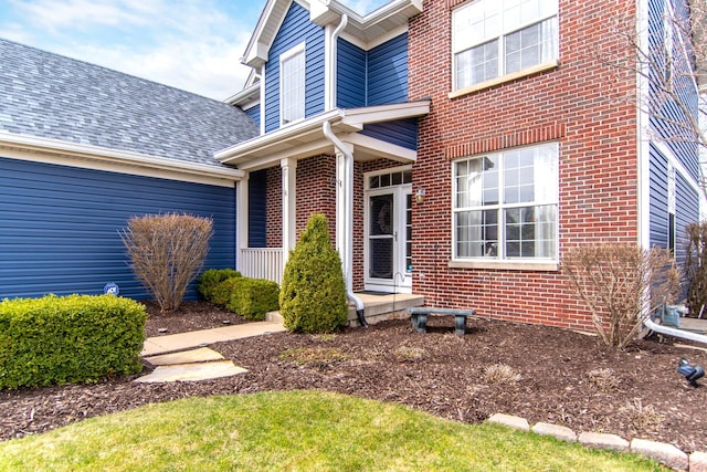 entrance to property featuring brick siding and a shingled roof