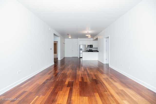unfurnished living room with dark wood-style flooring and baseboards