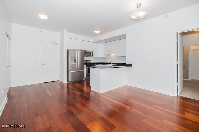 kitchen with appliances with stainless steel finishes, a peninsula, dark wood-style flooring, white cabinetry, and decorative backsplash