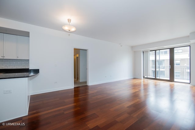 unfurnished living room with dark wood-style flooring and baseboards