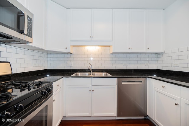 kitchen featuring appliances with stainless steel finishes, a sink, dark countertops, white cabinetry, and backsplash