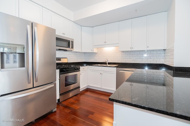 kitchen with appliances with stainless steel finishes, a sink, dark stone countertops, tasteful backsplash, and white cabinetry