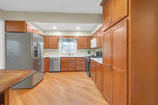 kitchen with appliances with stainless steel finishes, a sink, light wood-type flooring, and brown cabinetry