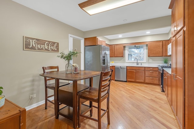 kitchen with appliances with stainless steel finishes, brown cabinetry, a sink, and light wood-type flooring
