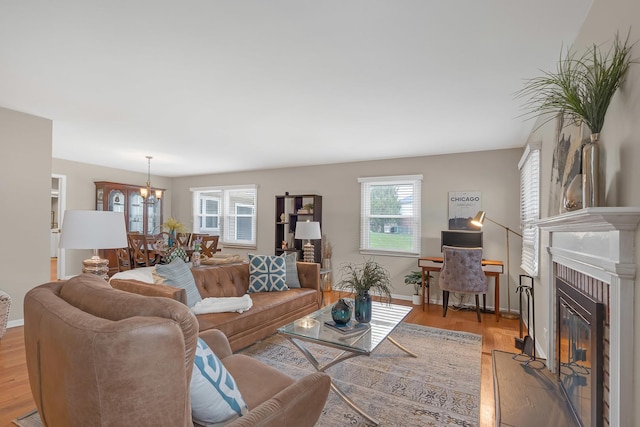 living room featuring a chandelier, a fireplace with flush hearth, light wood-type flooring, and baseboards