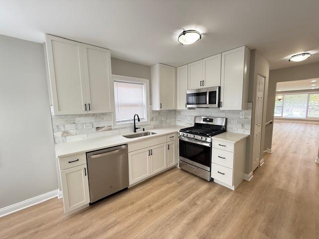 kitchen featuring appliances with stainless steel finishes, a sink, light wood-type flooring, and light countertops