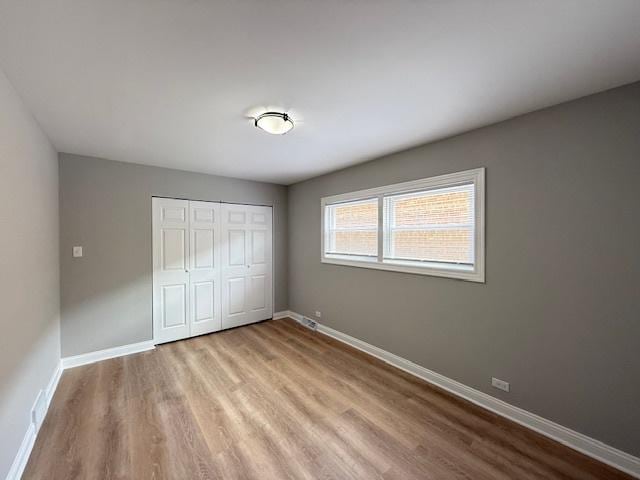 unfurnished bedroom featuring wood finished floors, baseboards, and a closet