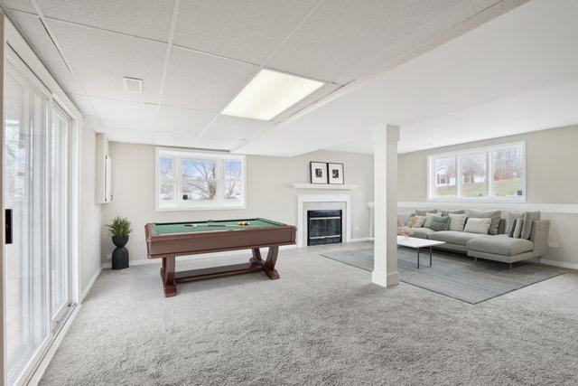 playroom featuring carpet flooring, pool table, a drop ceiling, plenty of natural light, and a glass covered fireplace