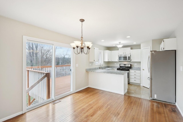 kitchen featuring stainless steel appliances, a sink, a peninsula, a chandelier, and light wood-style floors