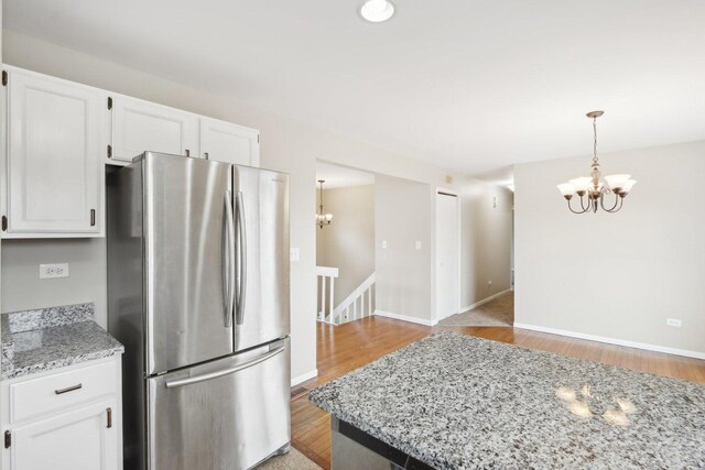 kitchen featuring freestanding refrigerator, a chandelier, white cabinetry, and light stone counters