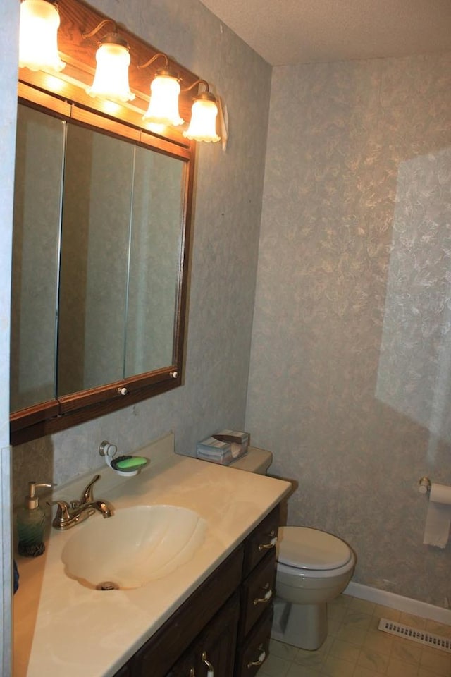 bathroom with vanity, toilet, wallpapered walls, and baseboards