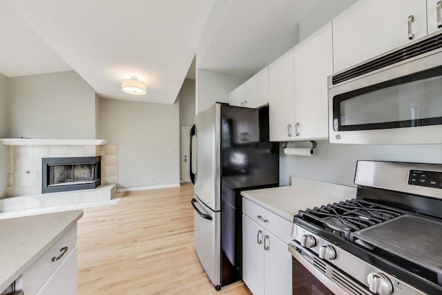 2136 W Evergreen Ave Unit 3B, Chicago, IL 60622 - kitchen featuring stainless steel appliances, light wood-type flooring, white cabinets, and a tile fireplace