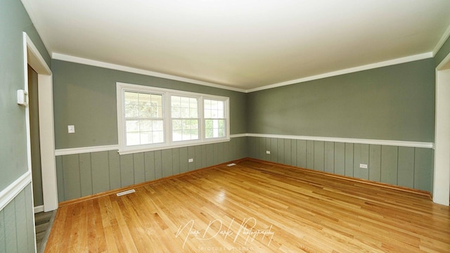 empty room with wood finished floors, a wainscoted wall, and ornamental molding