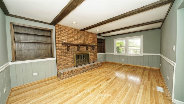unfurnished living room featuring wood-type flooring, wainscoting, beam ceiling, a fireplace, and wood walls
