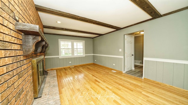 unfurnished living room featuring a brick fireplace, hardwood / wood-style flooring, a wainscoted wall, and beamed ceiling