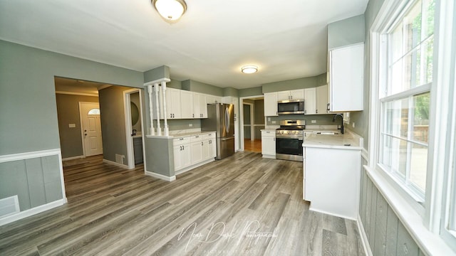 kitchen featuring appliances with stainless steel finishes, a sink, white cabinetry, wood finished floors, and healthy amount of natural light