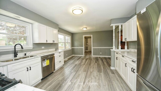 kitchen featuring stainless steel appliances, a sink, a wainscoted wall, white cabinets, and light wood-type flooring