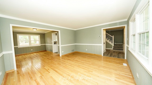 empty room with wood finished floors, stairway, a wainscoted wall, and crown molding