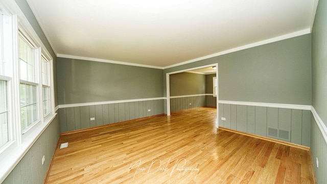 spare room with wood finished floors, a wainscoted wall, and ornamental molding