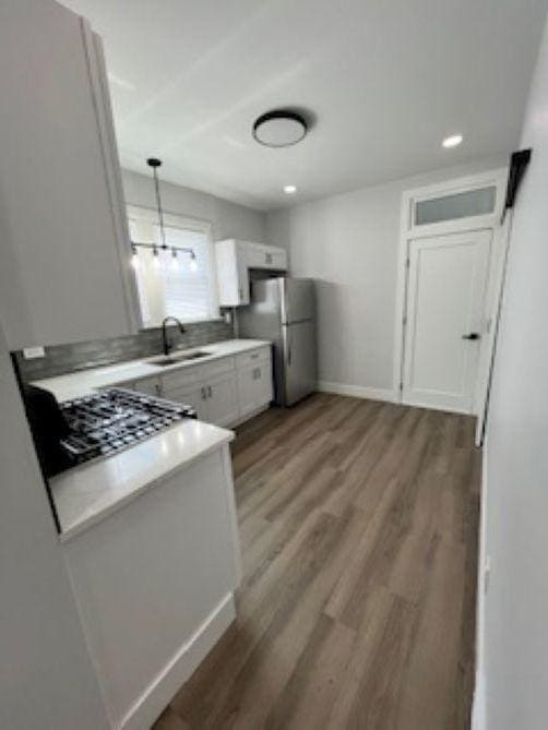 kitchen featuring a sink, freestanding refrigerator, light wood-style floors, white cabinets, and light countertops