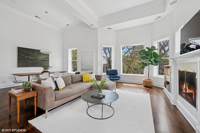 living room featuring dark wood finished floors, a glass covered fireplace, a towering ceiling, crown molding, and baseboards